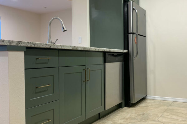 A modern kitchen with green cabinets, stainless steel appliances, a marble countertop, tile flooring, and two pendant lights hanging from the ceiling.